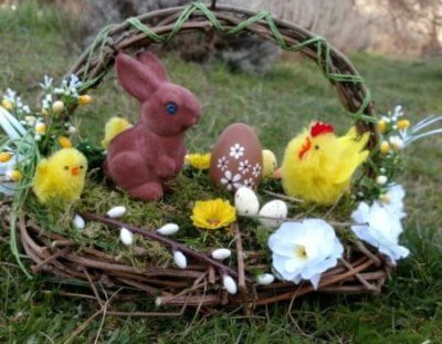 Koszyk wielkanocny zawierający króliczka, małą brązową pisankę i trzy żółte pisklęta. Wszystko w koszyku wielkanocnym z trawą w tle.