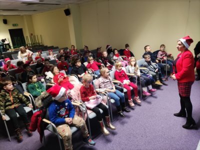 Grupa dzieci słuchających Mikołaja na sali konferencyjnej.