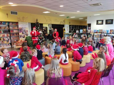 Grupa dzieci siedząca na pufach i słuchająca mikołaja.