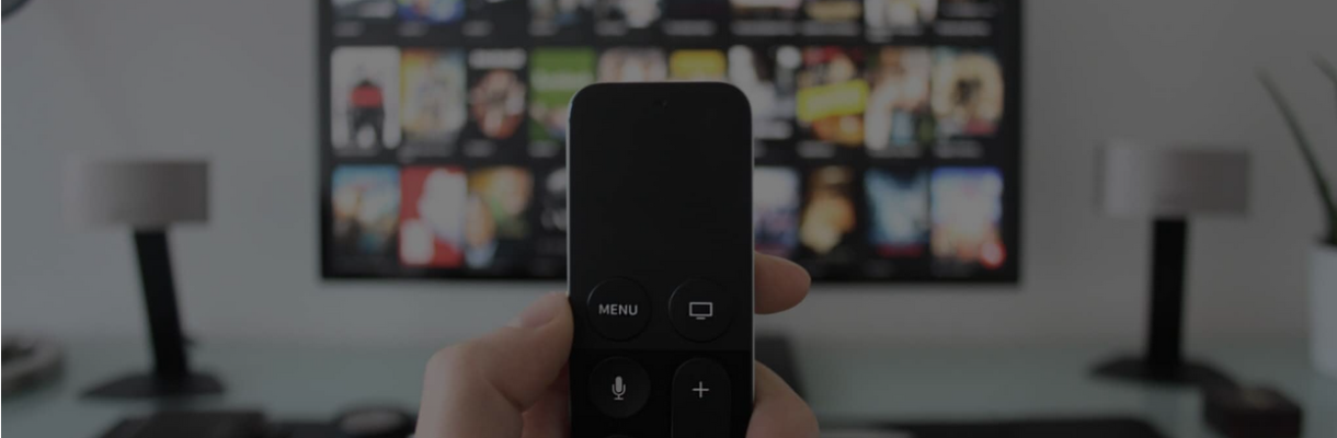 Zdjęcie - Pilot od telewizora trzymany w ręce, a w tle telewizor z telewizją na życzenie.