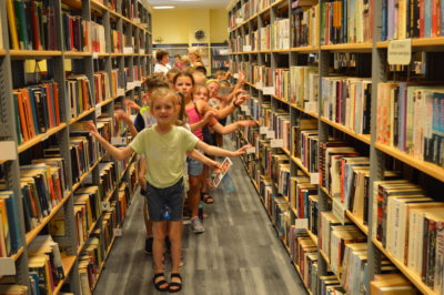 Dzieci z półkolonii przyjmujące pozę ptaka w otoczeniu regałów z książkami