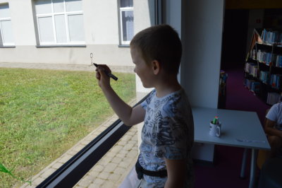 Chłopiec - uczestnik zabawy kalambury, rysuje na szybie wylosowane hasło