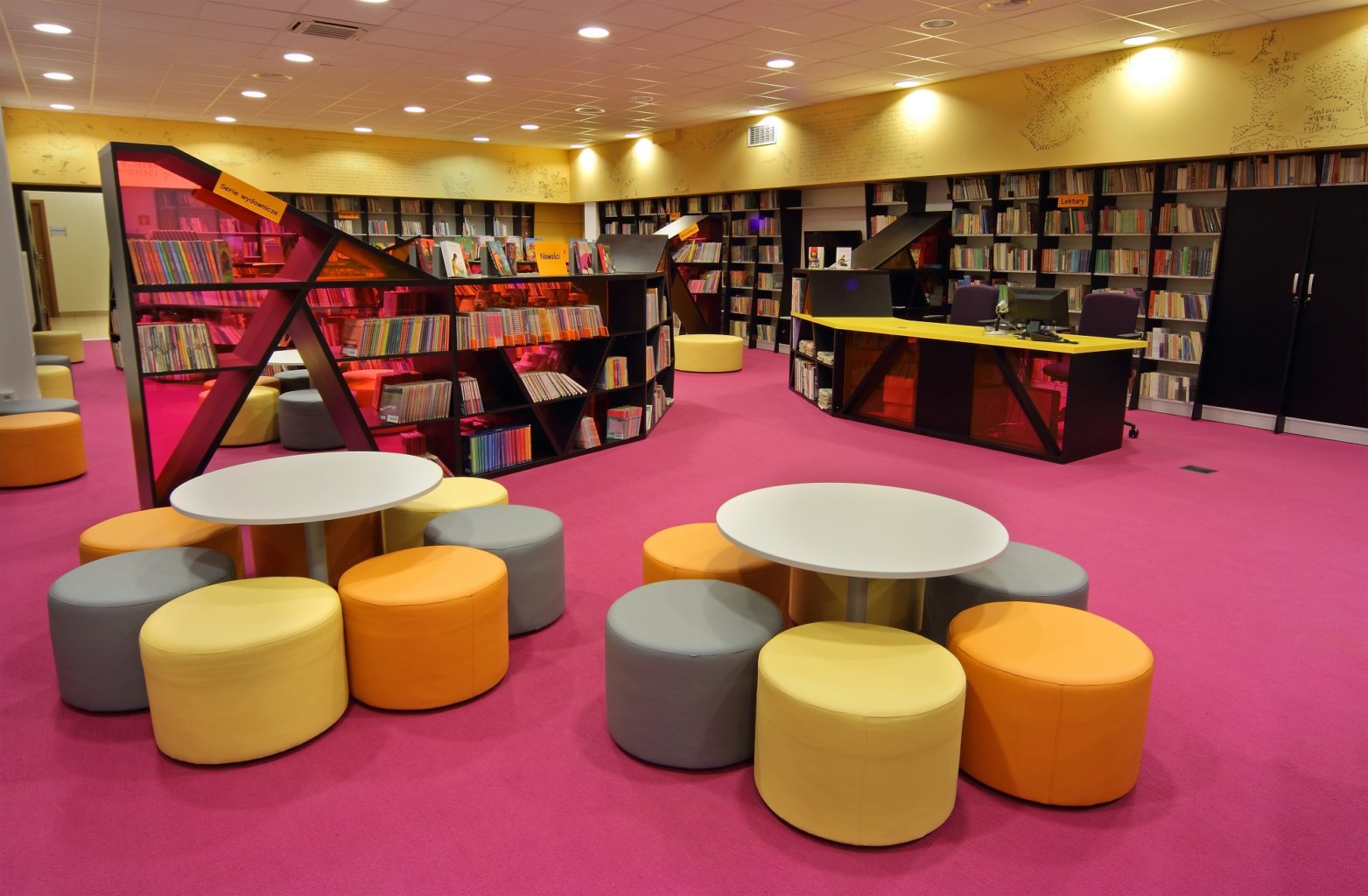 Pufy w czytelni dziecięcej na tle czytelni i książek.