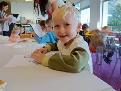 Uśmiechnięte dziecko koloruje kolorowankę.