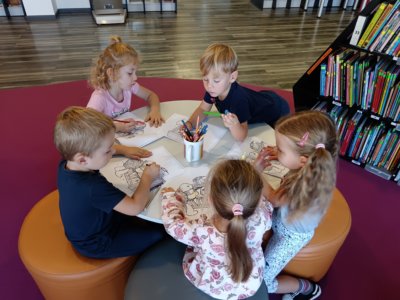 Dzieci przy okrągłym stole kolorują kolorowankę.