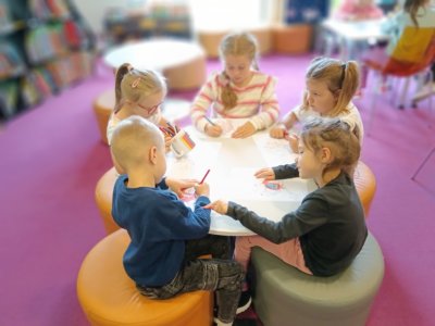 Dzieci przy okrągłym stole kolorują kolorowankę.