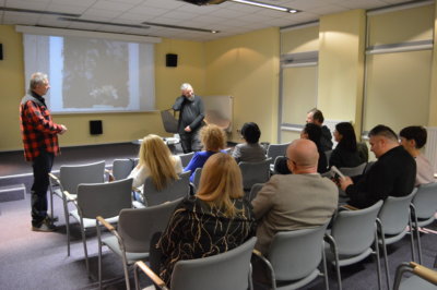 Ludzie na sali konferencyjnej słuchającyt Rroberta Gmiterek.