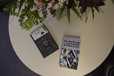 Dwie książki na stole obok wazonu kwiatów.