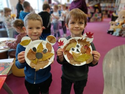 Dwóch chłopców trzymających wizerunek misia zrobiony z liści i papierowych talerzy.