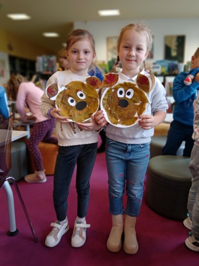 Dwie dziewczynki trzymających wizerunek misia zrobiony z liści i papierowych talerzy.