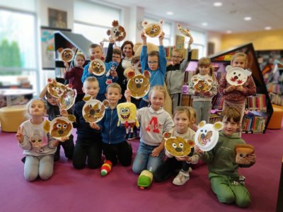 Grupa dzieci trzymających wizerunek misia zrobiony z liści i papierowych talerzy.