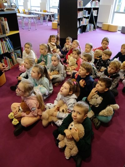 Grupa dzieci siedzących na ziemi z pluszowymi misiami.