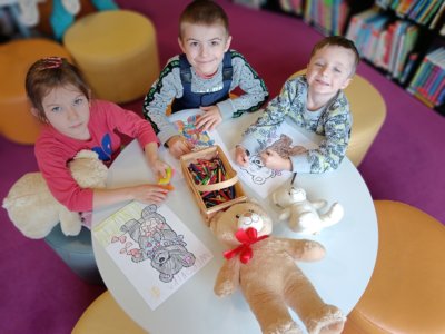 Troje dzieci koloruję kolorowankę przedstawiającą misia.