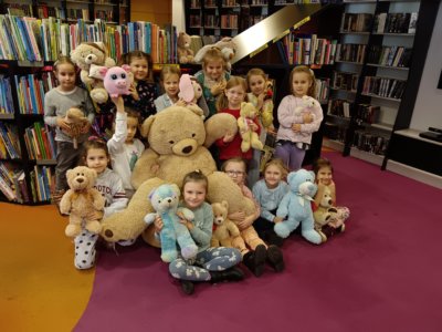 Dzieci podczas zajęć w bibliotece pozujące do zdjęcia z dużym pluszowym misiem.