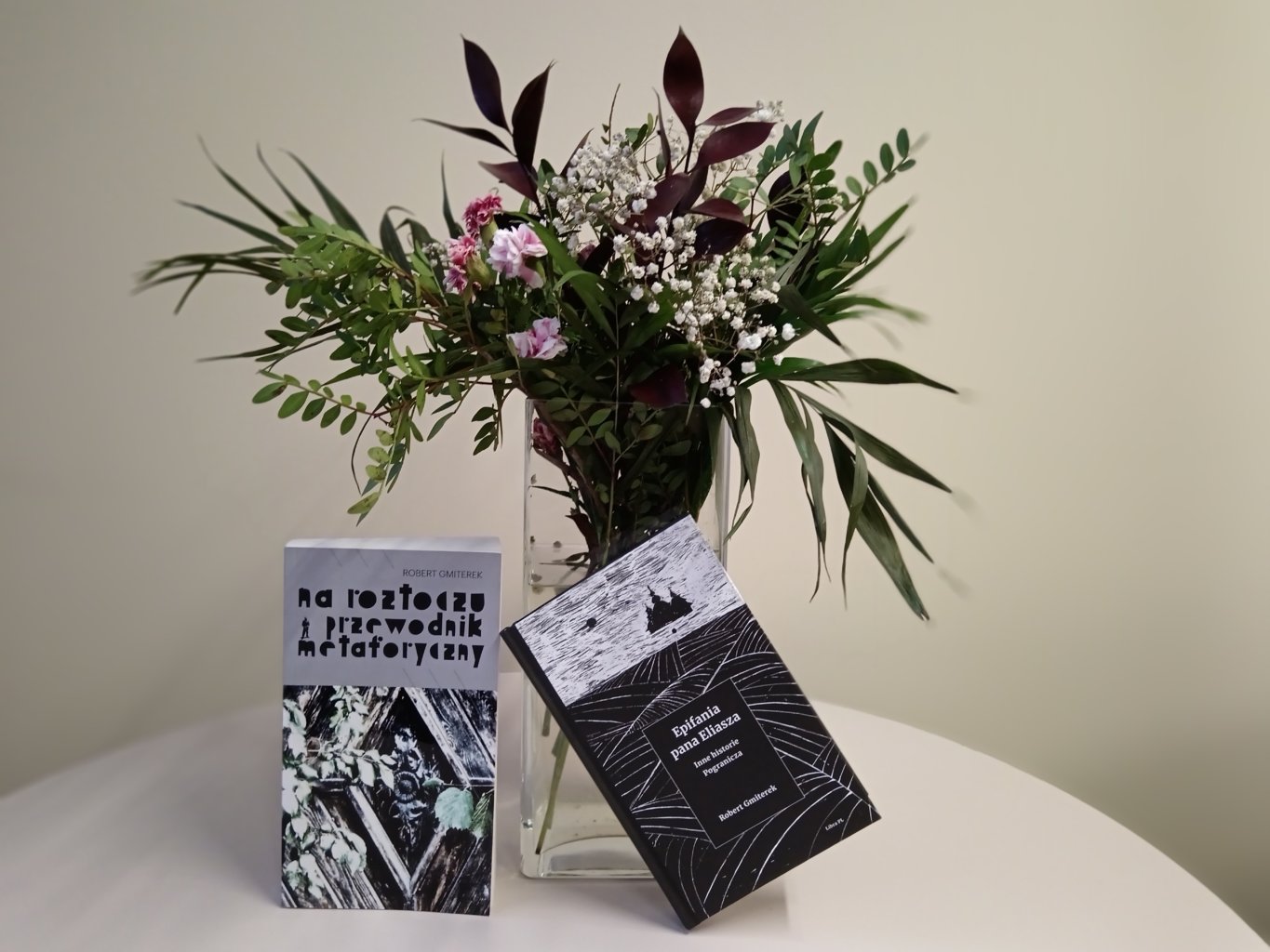 Dwie książki oparte o wazon kwiatów.