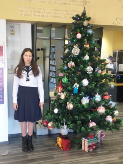 Dziewczyna pozuję do zdjęcia obok choinki.