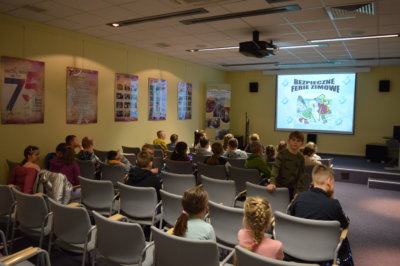 Dzieci na sali konferencyjnej oglądających animacje pod tytułem: Bezpieczne Ferie Zimowe.