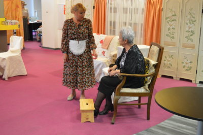 Dwie kobiety, jedna siedzi druga stoi tuż obok - fragment spektaklu Dom Kobiet w wykonaniu grupy Teatru Baccalaureus.