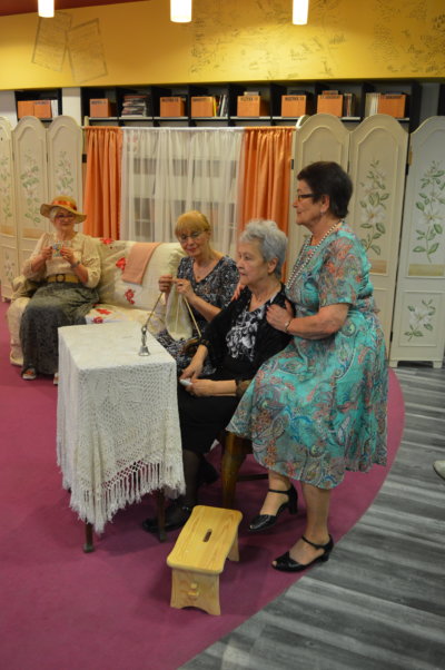 Cztery kobiety siedzą przy nakrytym na biało stole - fragment spektaklu Dom Kobiet w wykonaniu grupy Teatru Baccalaureus.